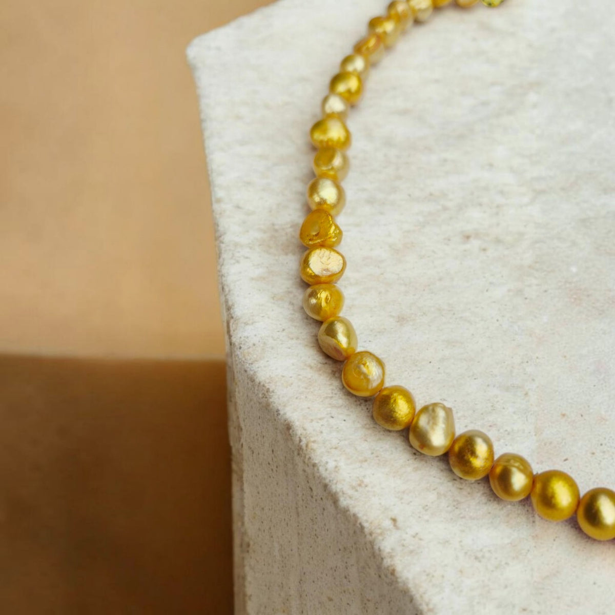 Detalle de collar de perlas de río teñidas de amarillo, con formas irregulares, sobre una base de piedra clara.